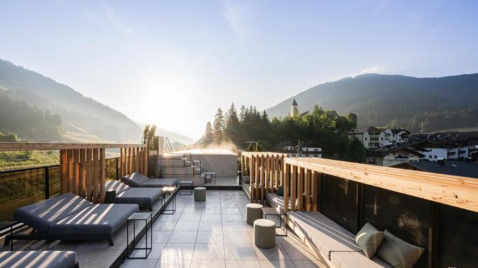Terrazza panoramica dell’Hotel Löwe con lettini e idromassaggio, con case, colline boscose e cielo azzurro sullo sfondo.