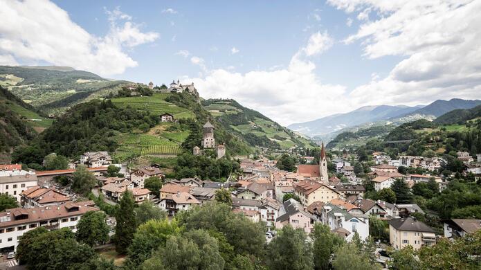 Blick auf die Stadt Klausen mit hügeliger Landschaft und blauem Himmel im Hintergrund.