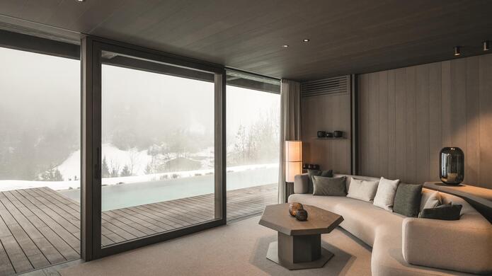 Wohnraum mit großer Fensterfront und Blick auf den Außenpool und die schneebedeckte Landschaft.