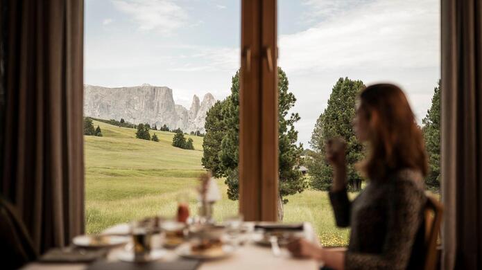 Ristorante Steger Dellai sull’Alpe di Siusi con ambiente accogliente e vista sul paesaggio alpino con prati verdi e montagne sullo sfondo.