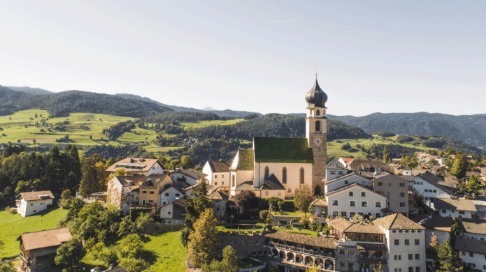 Panoramablick auf das Hotel Turm mit Dorf, Häusern umgeben von grünen Wiesen und Wald im Hintergrund.