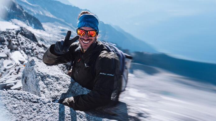 Persona con maschera da sci e abbigliamento invernale in un paesaggio montano innevato.