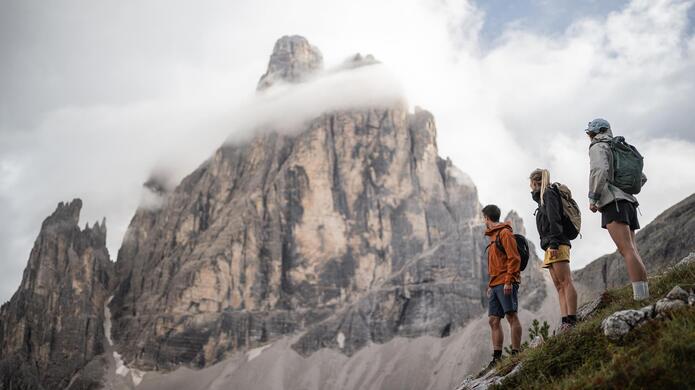 Escursionisti su un sentiero alpino con le caratteristiche formazioni rocciose delle Dolomiti di Sesto sullo sfondo.