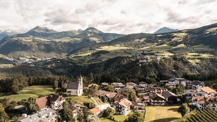 Blick auf Natz-Schabs mit hügeliger Landschaft, weiteren Dörfern und Bergen im Hintergrund .