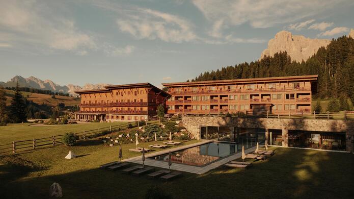 Hotel Floralpina al tramonto con prato, piscina e paesaggio montano sullo sfondo.
