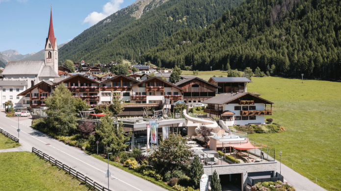 Ansicht Hotel Huber umgeben von Wiesen, Wald und Bergen im Hintergrund.