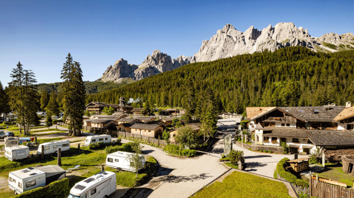 Vista panoramica del Caravan Park Sexten con camper e piazzole immersi in un paesaggio verde, con un’imponente cornice montana e cielo azzurro sullo sfondo.