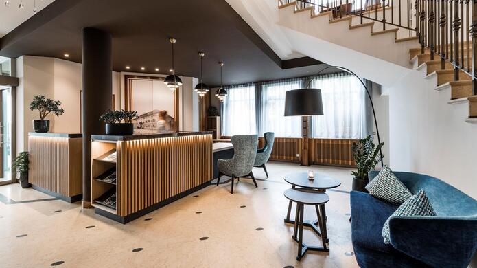 Hotel Post al Plan de Corones con area salotto e scala in un ambiente interno elegante con grandi finestre e arredamento luminoso.
